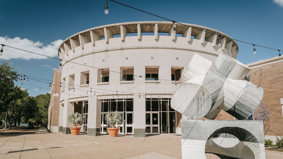 A modern building with a circular design, large windows, and a prominent sculpture in front.