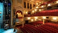An ornate theater with red seats and a stage.