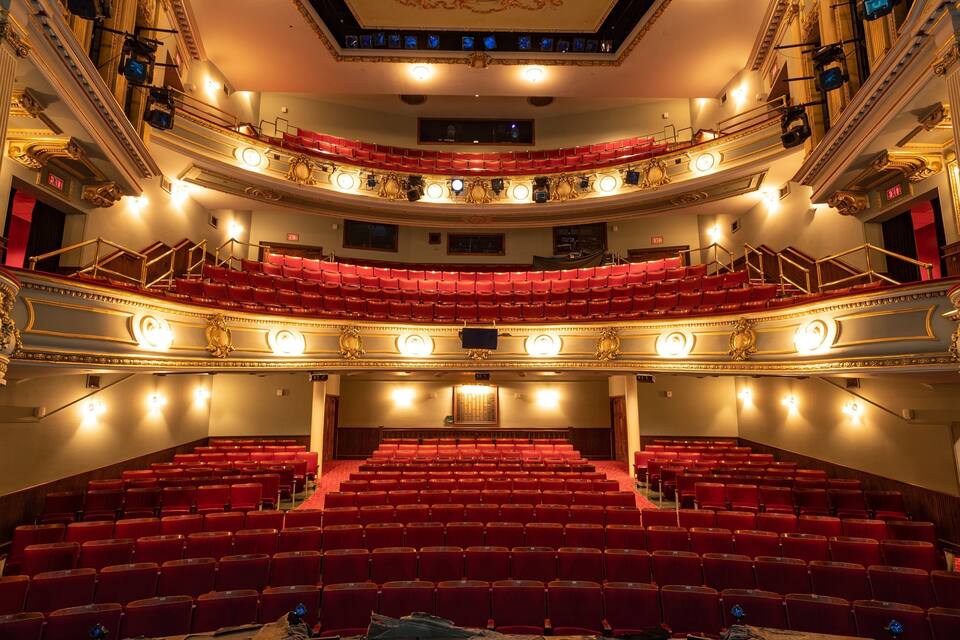 An ornate theater with red seats and a balcony.