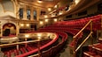A grand theater with red velvet seats, ornate gold detailing, and a central stage.