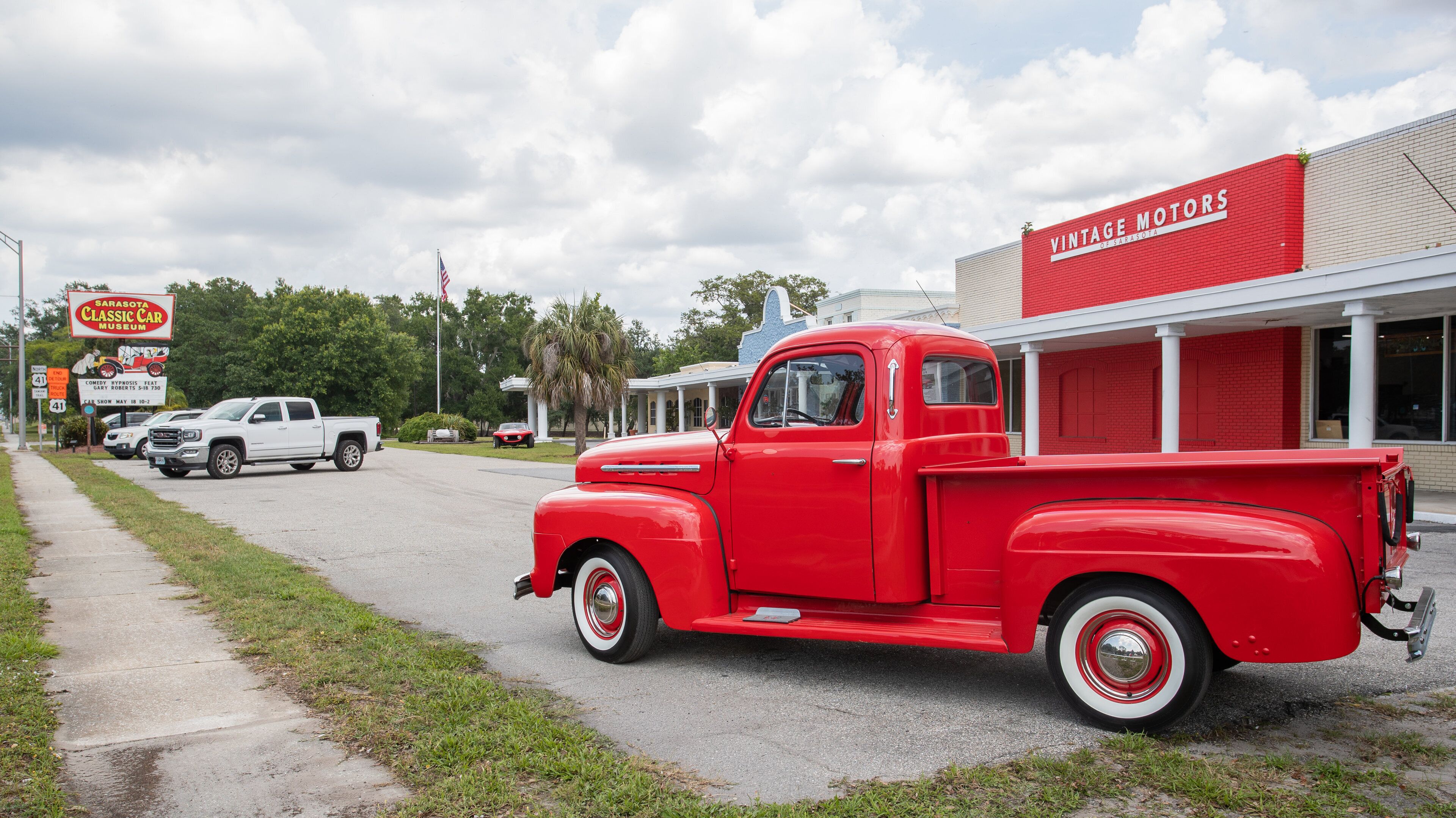 A red vintage truck parked in front of a building with a red sign that reads "Vintage Motors."