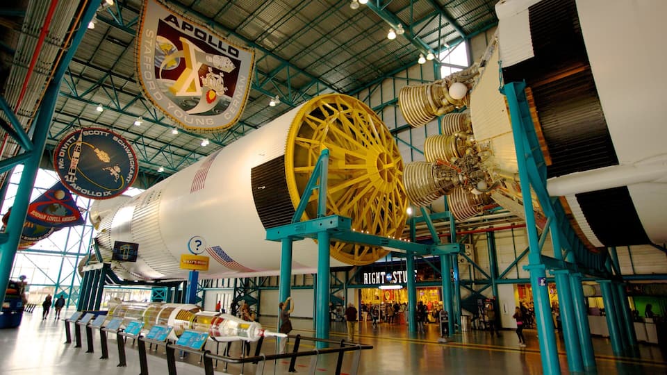 A space shuttle on display in a museum with informational signs and a large yellow wheel structure.