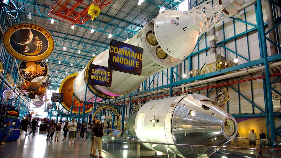 A space shuttle on display in a museum with various space mission plaques and a large circular structure.