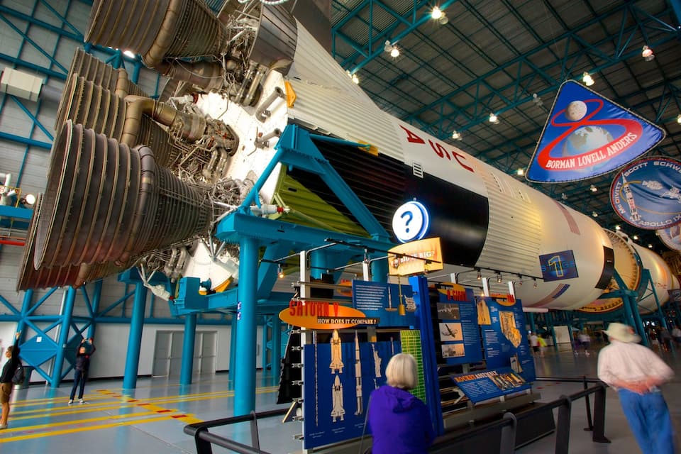 Uma grande nave espacial em exposição em um museu, com placas informativas e visitantes ao redor.