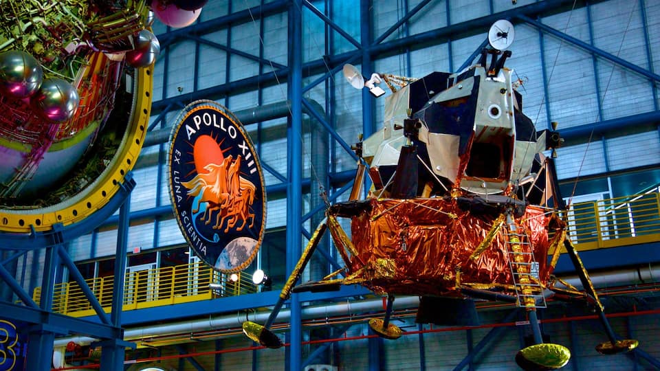 A space shuttle on display at a museum, surrounded by a large blue metal framework.