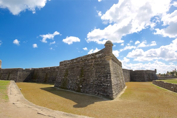 A historic stone fort with a prominent tower, surrounded by grassy areas and under a partly cloudy sky.