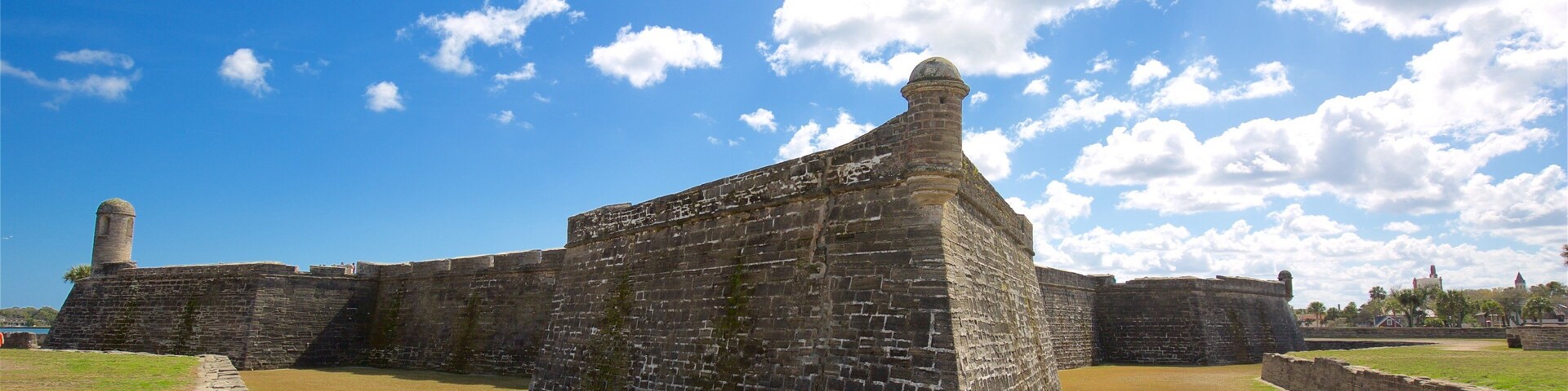 A historic stone fort with a prominent tower, surrounded by grassy areas and under a partly cloudy sky.