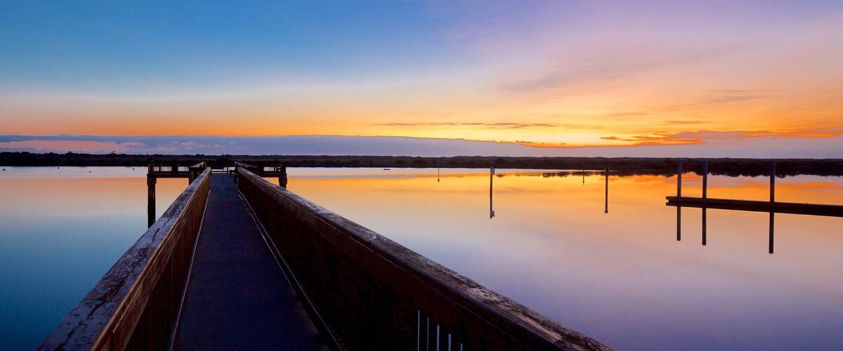 A wooden pier extending into calm water at sunset.