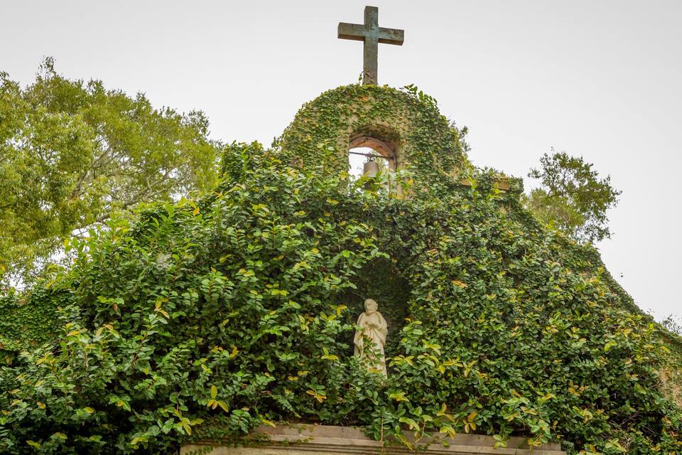 Església coberta d'heura amb una creu al capdamunt i una estàtua al davant.