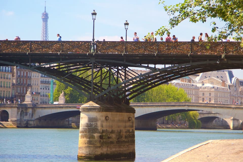 A bridge with pedestrians, a river, and historic buildings in the background.