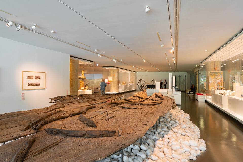 Eine Kunstgalerie im Innenbereich mit einer großen Holzskulptur und Glastauslagen.