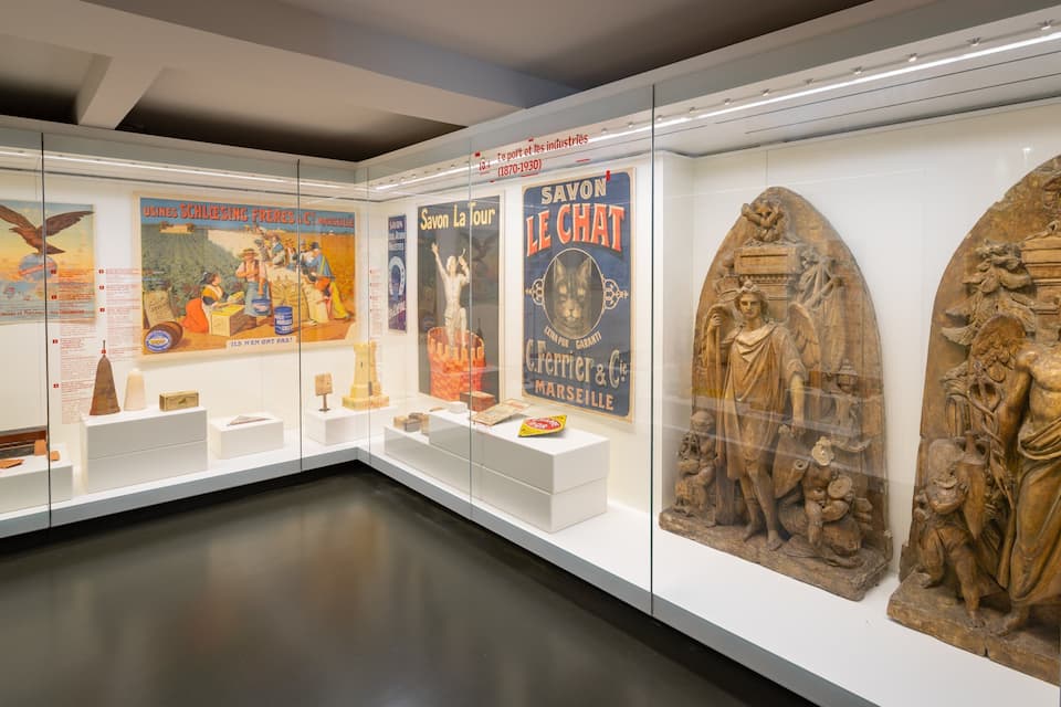 Una exposición de museo con carteles históricos, una maqueta de faro y esculturas clásicas.