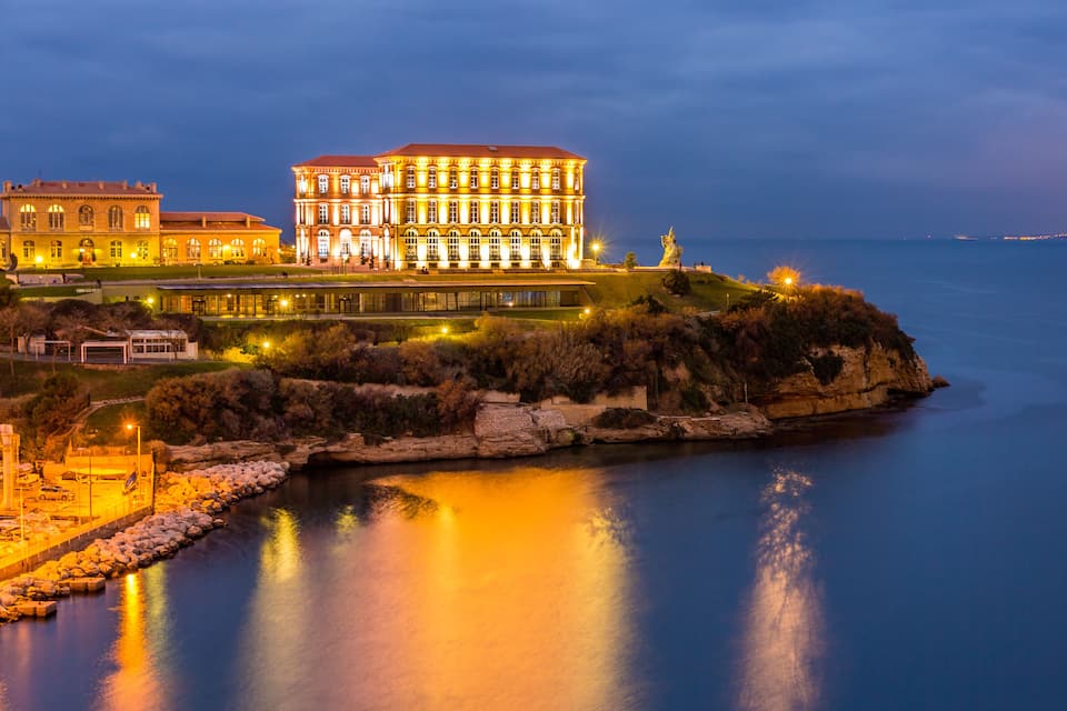 Um edifício imponente e iluminado à beira de águas calmas ao entardecer.