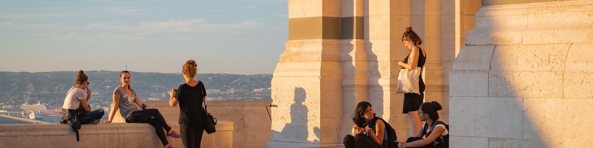 Un grupo de personas sentadas y de pie cerca de una gran estructura de piedra con columnas.