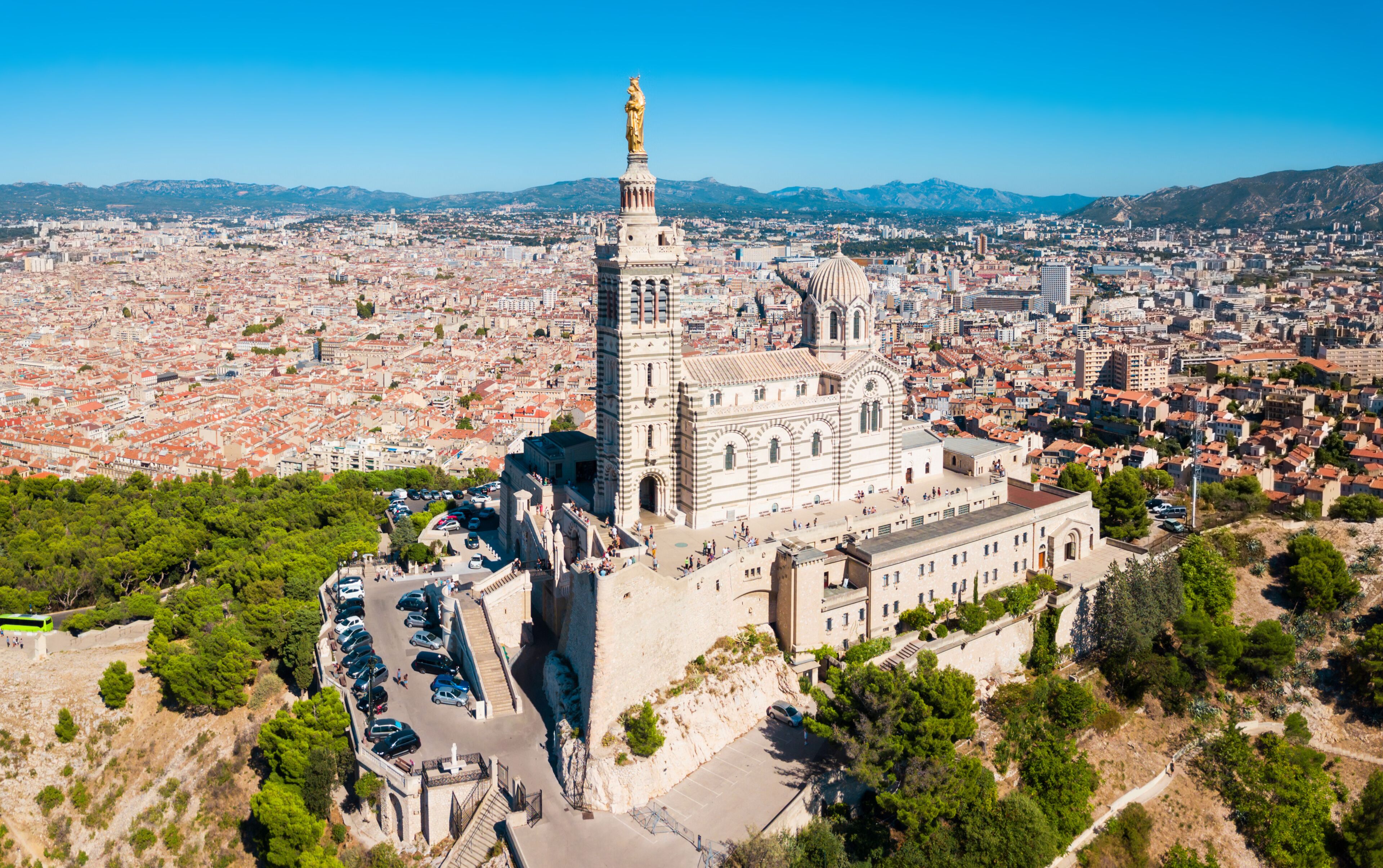 Una cattedrale con un'alta torre e una statua, immersa in un panorama urbano con montagne sullo sfondo.