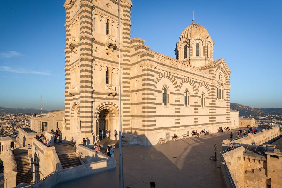 En stor katedral med ett markant torn och en kupol, omgiven av ett stort torg fullt av människor.