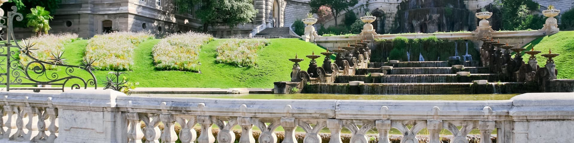 A grand building with ornate architecture, a large fountain, and well-manicured gardens.