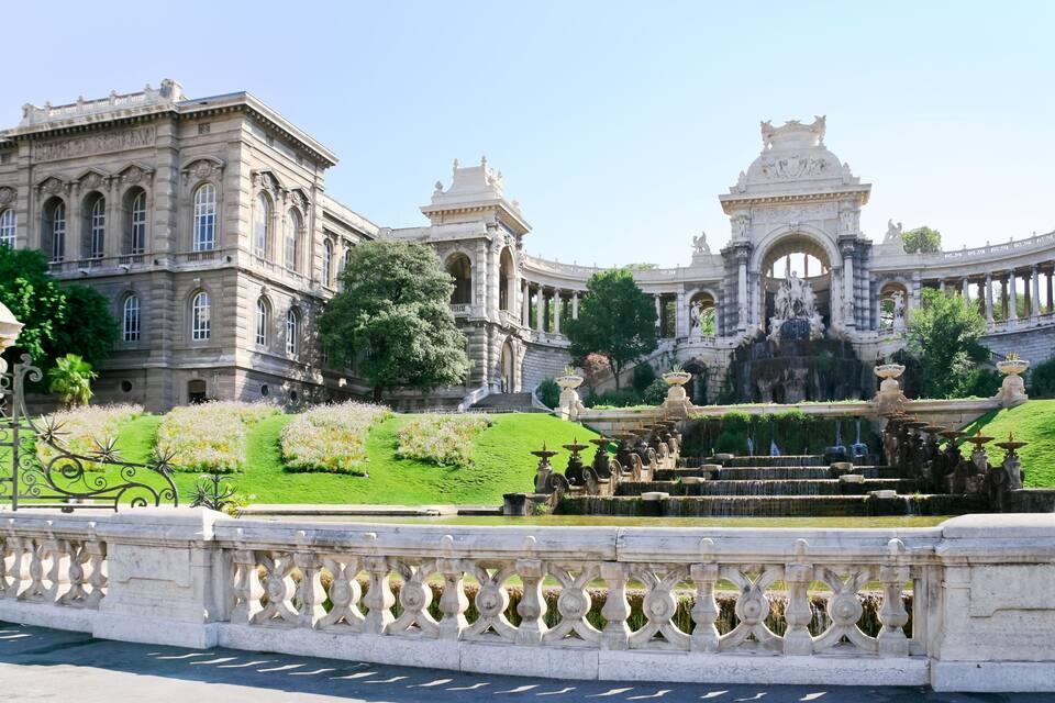 A grand building with ornate architecture, a large fountain, and well-manicured gardens.