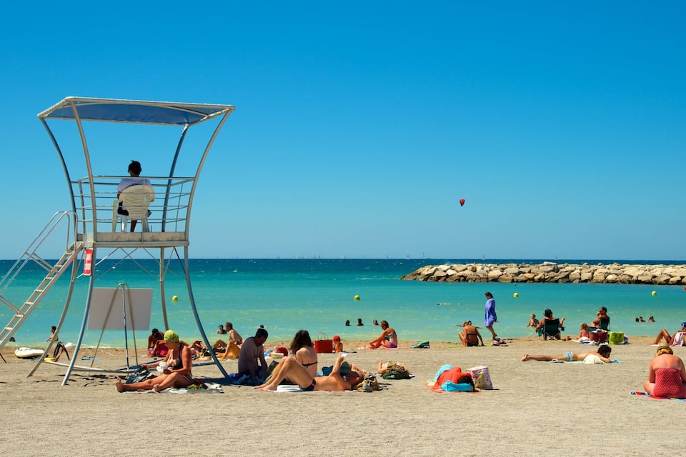 A beach with a lifeguard tower, clear turquoise water, and people sunbathing.