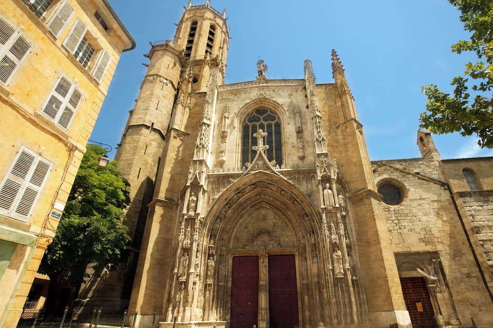 Uma catedral gótica com uma alta torre sineira, grandes janelas em arco e estátuas.