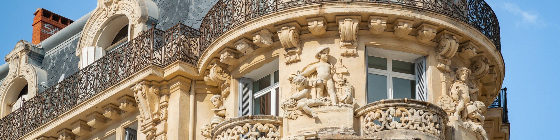 Detalhes arquitetônicos elaborados, incluindo esculturas e trabalhos em ferro decorativos na fachada de um edifício.