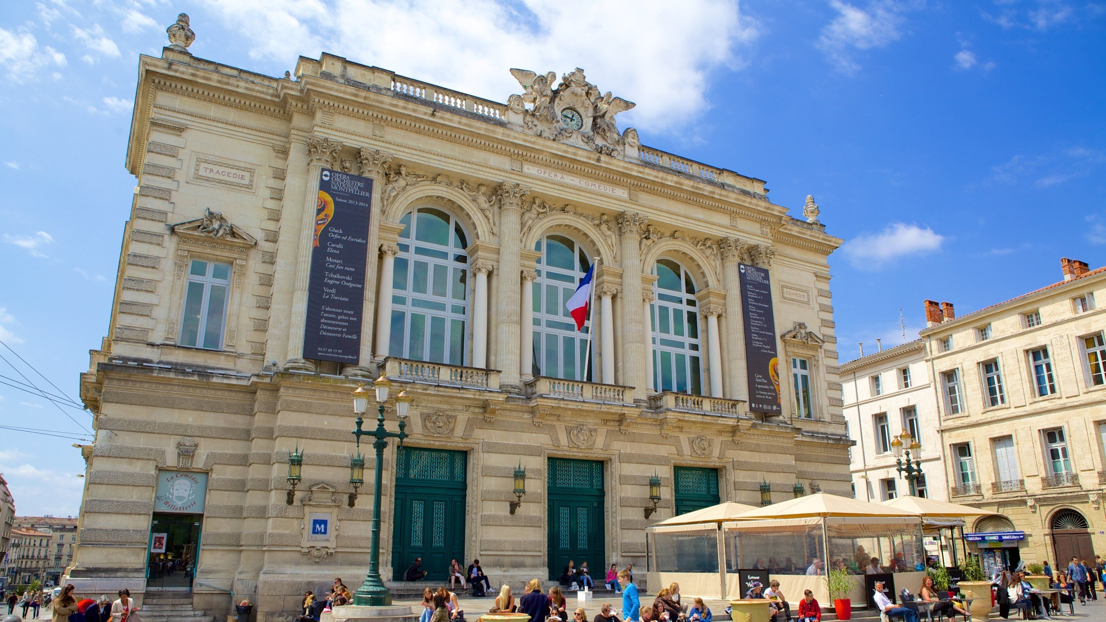 Un opéra historique à l’architecture riche et ornée, doté de portes vertes et arborant un drapeau.