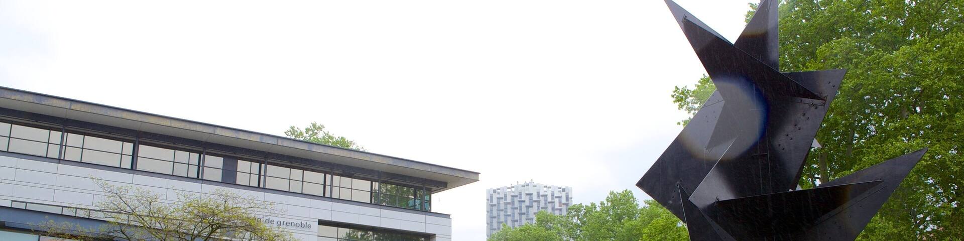 A modern building with a glass facade, a large abstract sculpture, and a staircase leading up to the entrance.