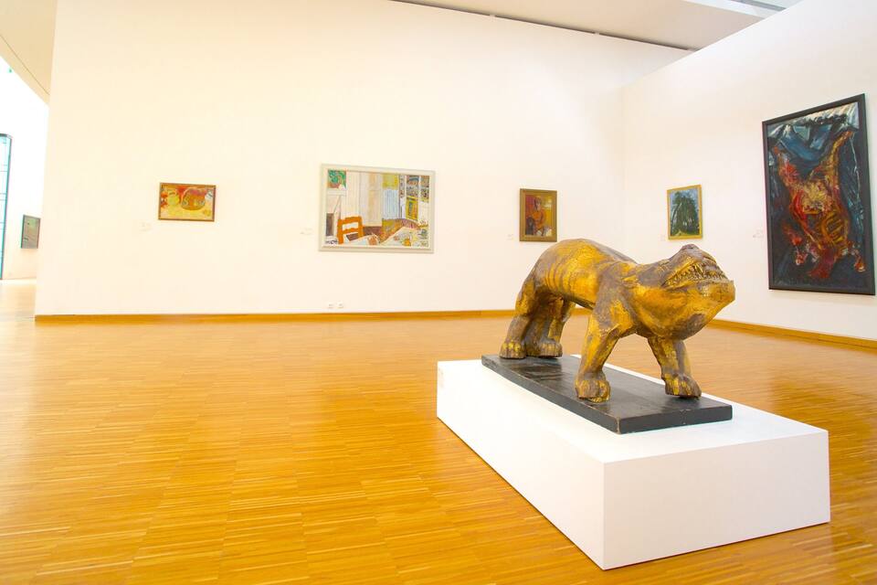 Uma galeria de arte com piso de madeira e diversas pinturas nas paredes.