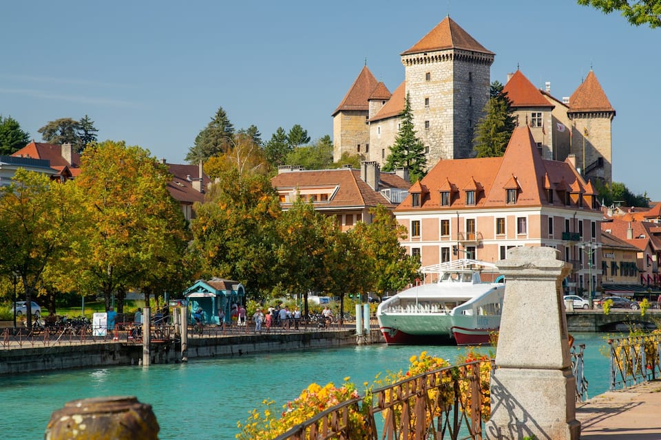 A riverside town with historic buildings, a castle, and a boat docked by the water.