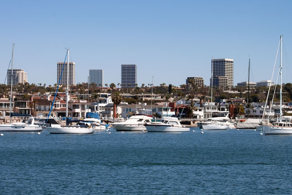 A marina with several yachts docked and a cityscape with tall buildings in the background.