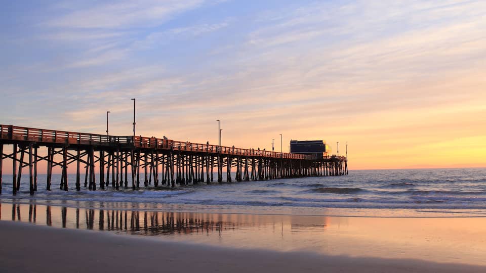 A pier extending into the ocean at sunset with calm waves and a clear sky.