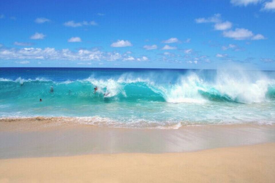 A beach with waves, clear sky, and a few people swimming.