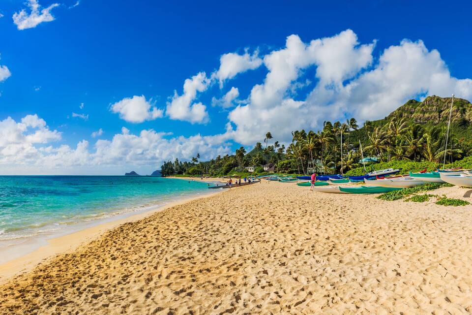 A beach with clear turquoise water, a sandy shore, and several boats lined up on the right.