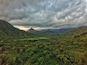 A lush valley with dense greenery, a river, and distant mountains under a cloudy sky.