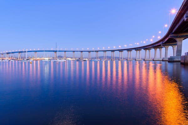 Eine Brücke über ruhiges Wasser, mit Booten und Stadtlichtern, die sich auf der Oberfläche spiegeln.