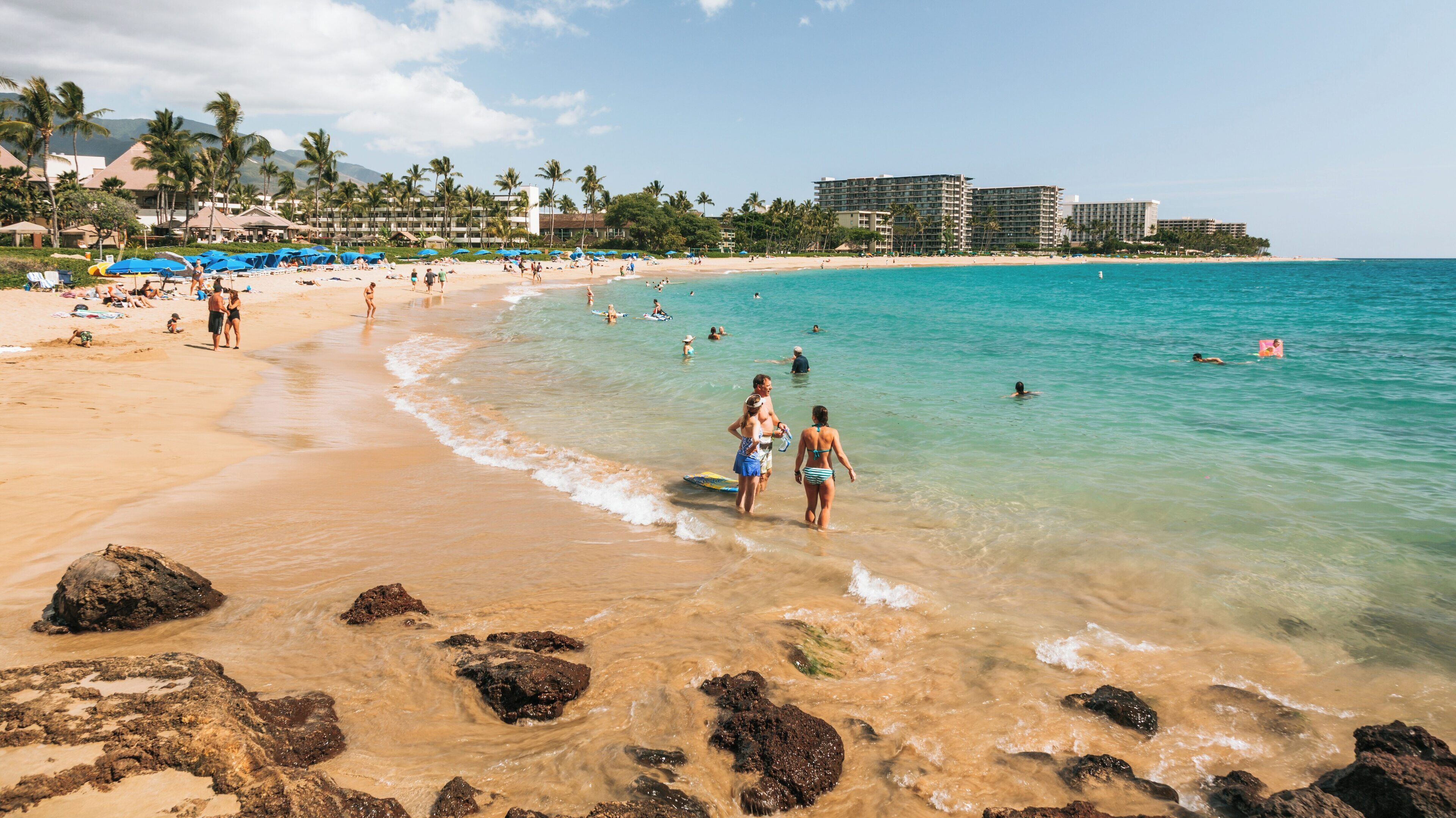Sunbathers enjoy a sunny day at Kaanapali Beach in Lahaina, Hawaii featuring clear waters and golden sand