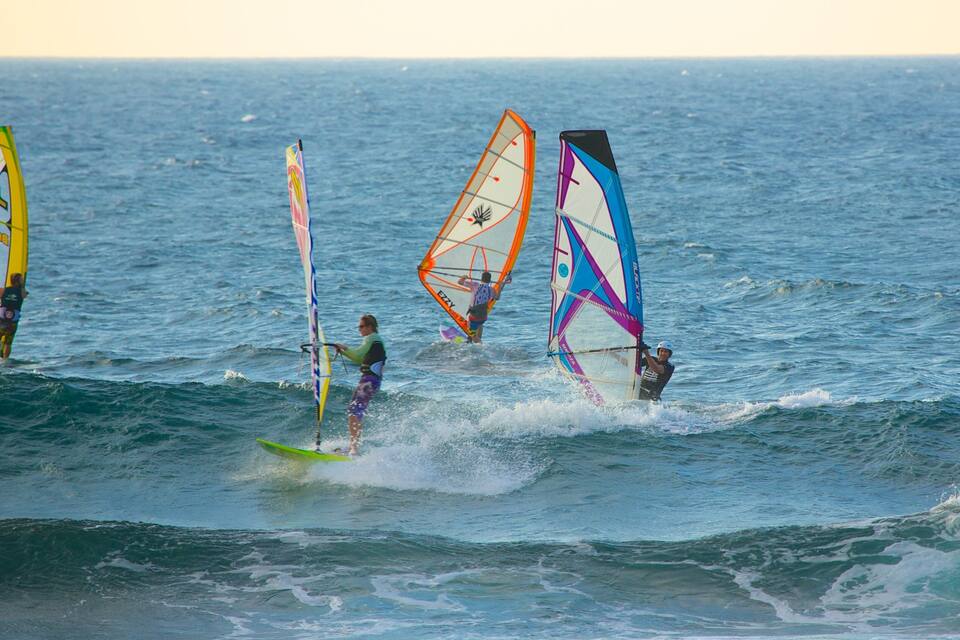 Drie windsurfers op een rustige zee, heldere lucht.