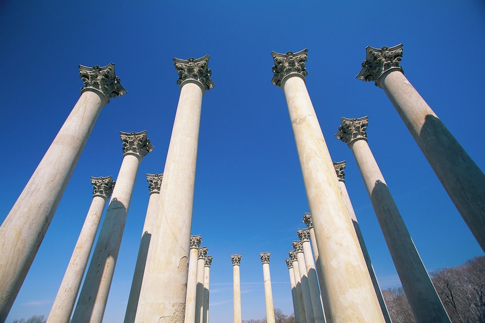 A series of tall, white columns with ornate capitals against a clear blue sky.
