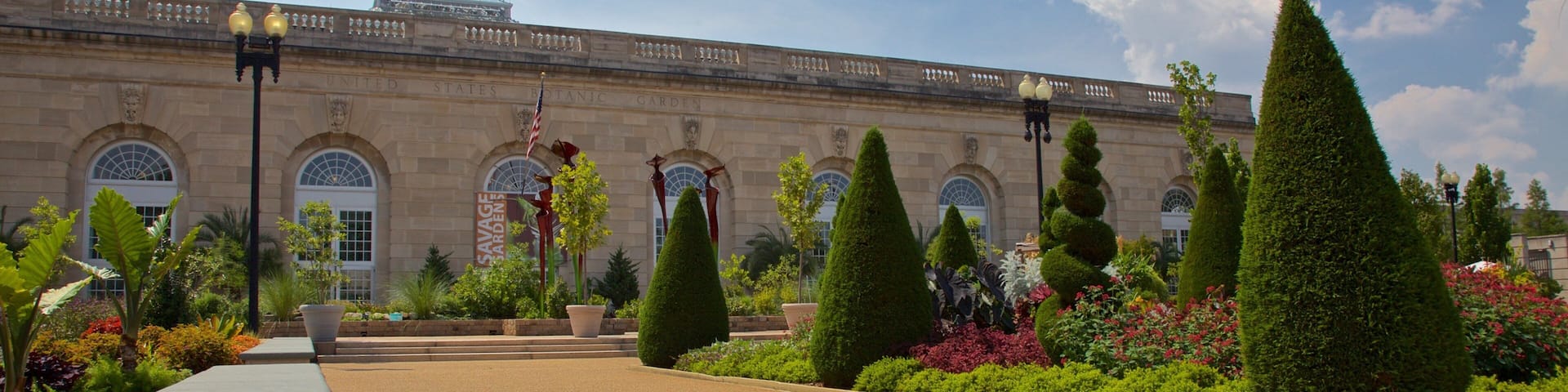 Un edificio histórico con un jardín formal, que incluye setos cuidadosamente podados y una variedad de flores coloridas.