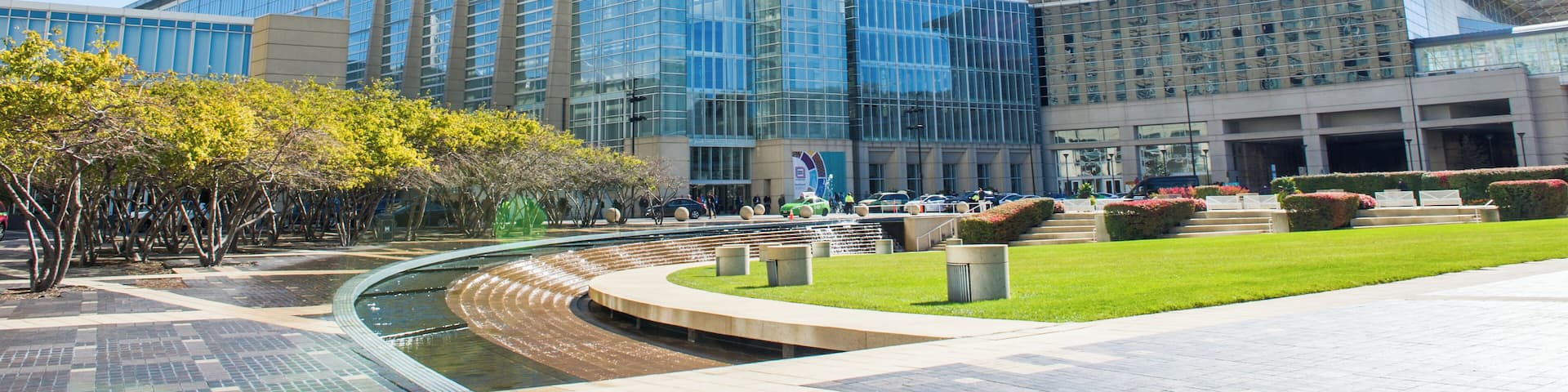 A modern glass building with a curved roof, surrounded by a landscaped garden and a water feature.
