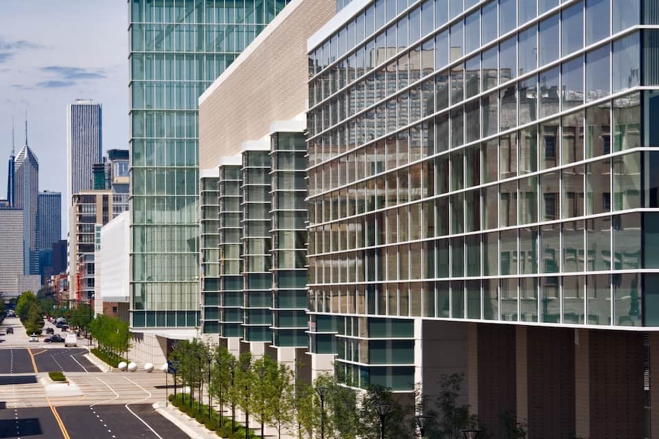 A modern cityscape with tall buildings, a clear sky, and a tree-lined street.