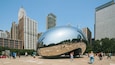 A large metallic sphere sculpture in a public square surrounded by tall buildings.