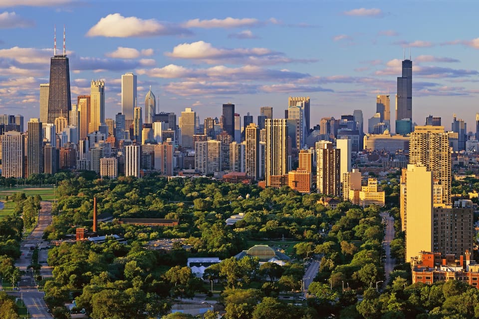 Un paysage urbain côtier avec de hauts immeubles, une marina et un espace vert aménagé en parc.
