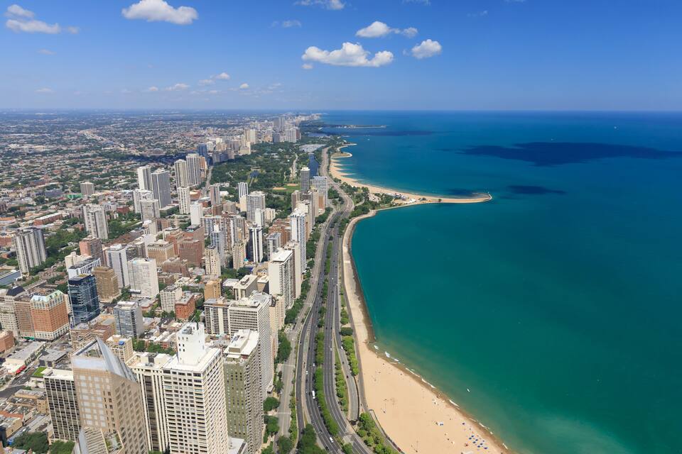 A coastal city with high-rise buildings, a curved beach, and a clear blue ocean.