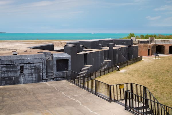 Uma fortificação costeira com uma escadaria que leva a uma plataforma mais alta, com vista para o mar.