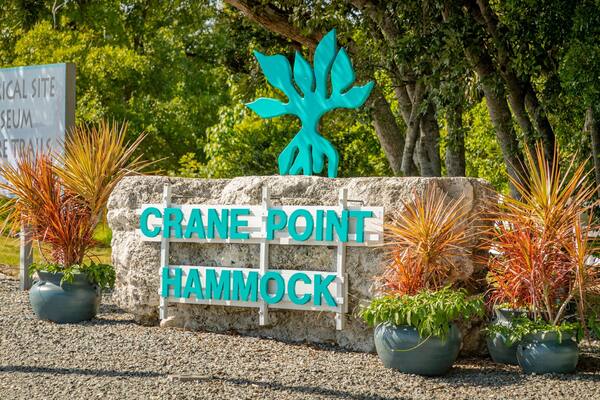 Un panneau indiquant l’entrée de Crane Point Hammock, avec un logo représentant un arbre et des plantes en pot.