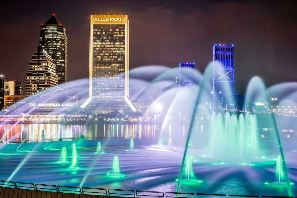 A city skyline with illuminated buildings and a water fountain display.