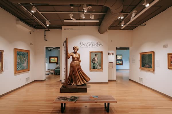 Une galerie d’art avec une statue centrale, des tableaux encadrés et des panneaux d’information.