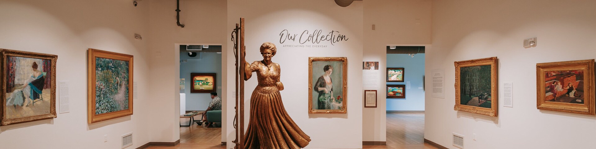 Uma galeria de arte com uma estátua central, pinturas emolduradas e placas informativas.