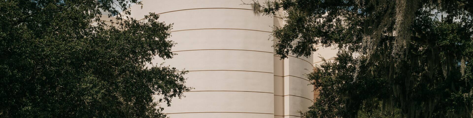 The Orlando Science Center with a large, curved building surrounded by trees and a well-maintained lawn.